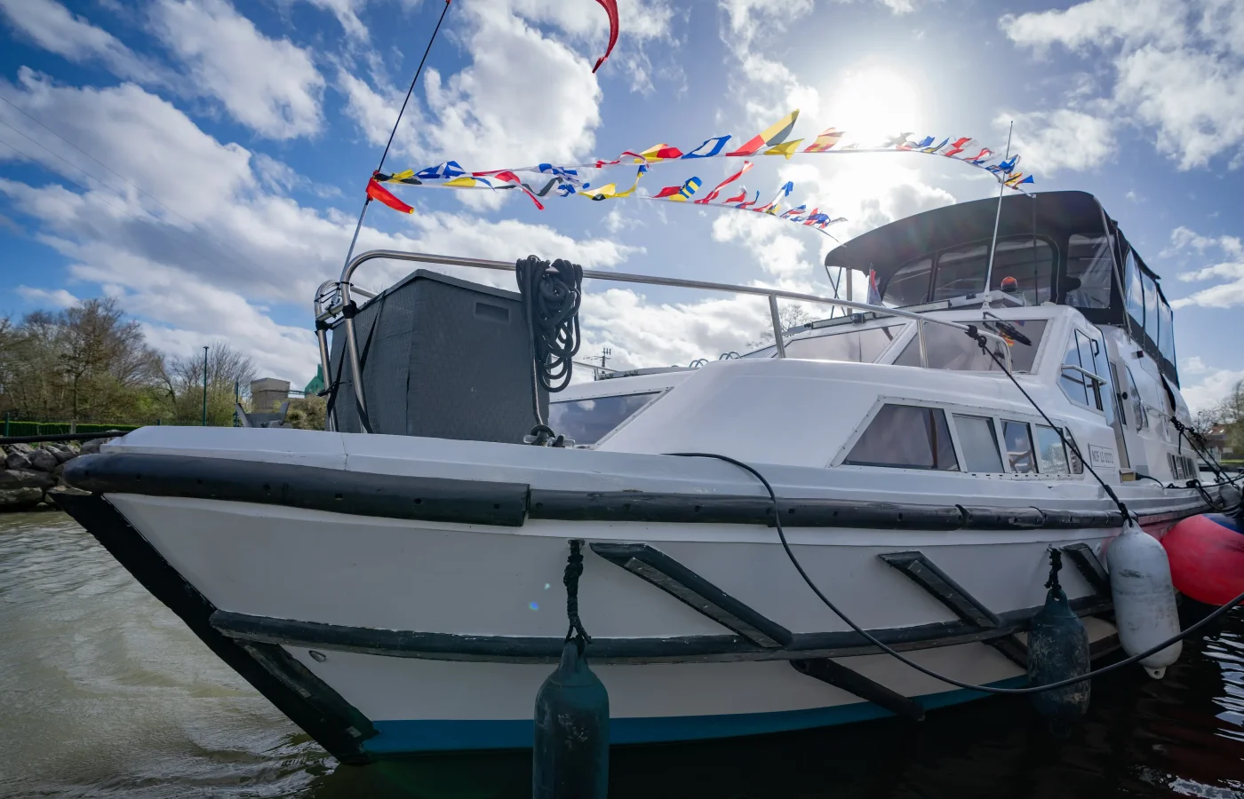 Bateau de plaisance blanc amarré au port fluvial d'Aire-sur-la-Lys avec drapeaux colorés